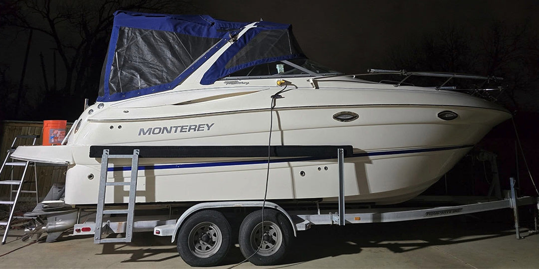 Side view of a Monterey cabin cruiser boat on a trailer at night, with a blue canopy partially covering the cockpit area.