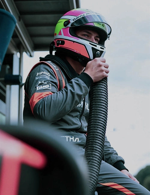 A racecar driver is holding an air cooling hose, staying cool and focused before a race.
