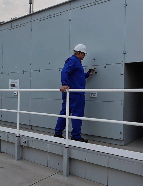 An HVAC technician in a blue protective uniform performs maintenance on a large industrial air conditioning unit.