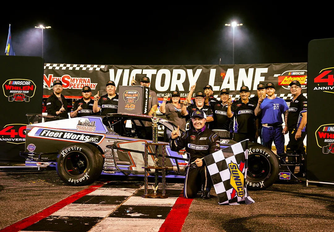 Patrick Emerling and his team celebrate in Victory Lane at New Smyrna Speedway with his race car, trophy, and a Sunoco checkered flag.