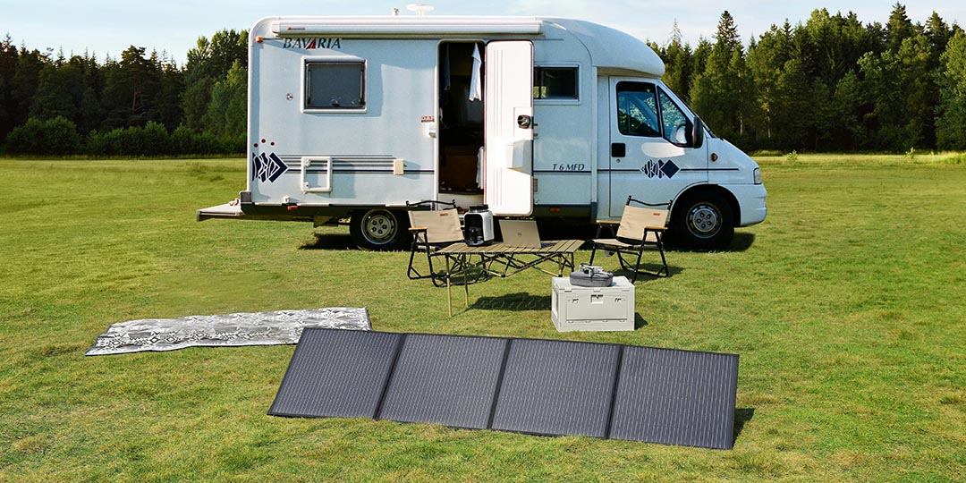 A white RV is parked on a grassy field with camping gear set up outside, including a foldable solar panel, illustrating an off-grid outdoor living setup.