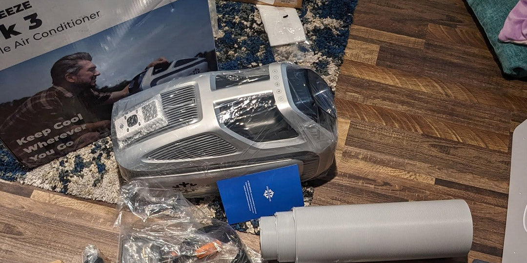 Unboxing the ZERO BREEZE Mark 3 portable air conditioner with included accessories, hose, and user manual displayed on the floor.