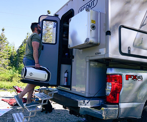 A man carries the portable air conditioner up the stairs into a truck camper, showing its lightweight and portable design ideal for off-grid adventures.