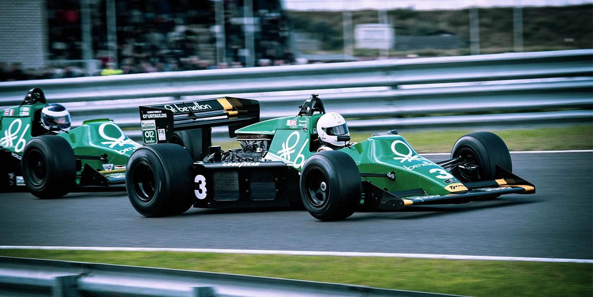 A vintage green Formula 1 racecar is competing on a track during a high-speed race.