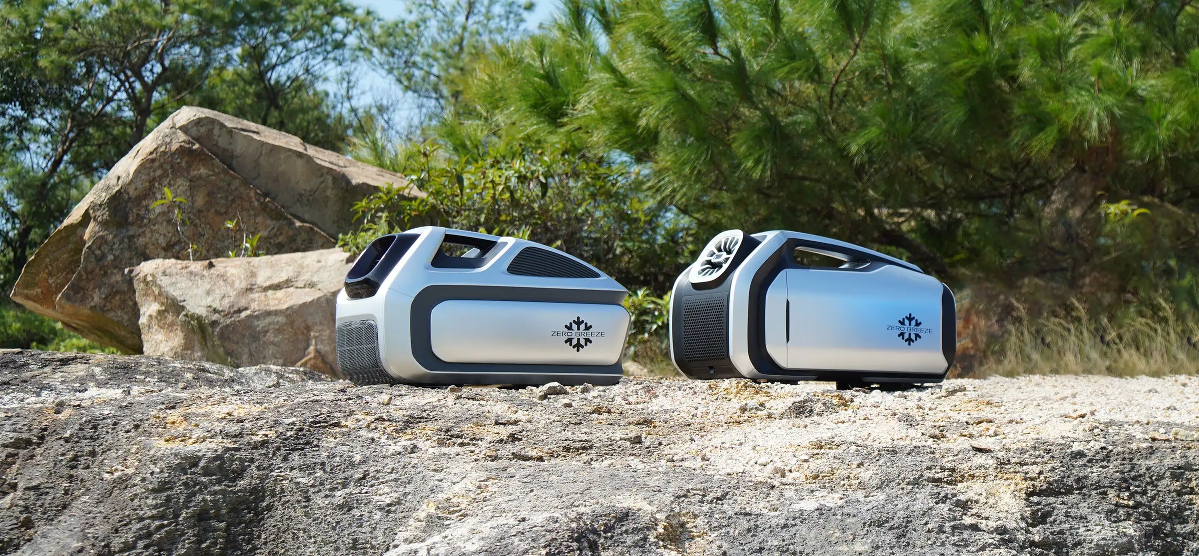 Side-by-side comparison of ZERO BREEZE Mark 2 and Mark 3 portable air conditioners placed outdoors on a rocky surface, surrounded by greenery and natural light.