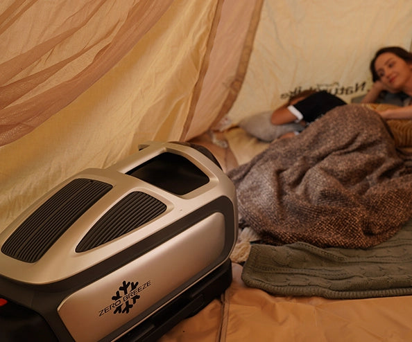A woman and a child relax in a tent with a ZERO BREEZE Mark 3 portable air conditioner blowing cool air towards them.